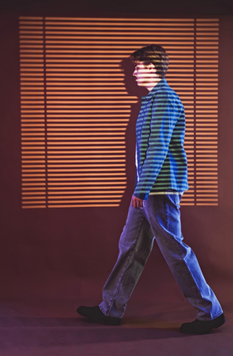 Morris Jones walking past a window, light falling through the blinds